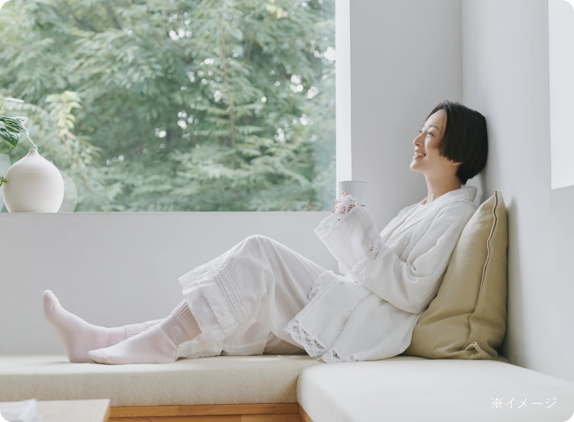 布団から出て窓辺で靴下を履いた足もとをくつろがせる様子